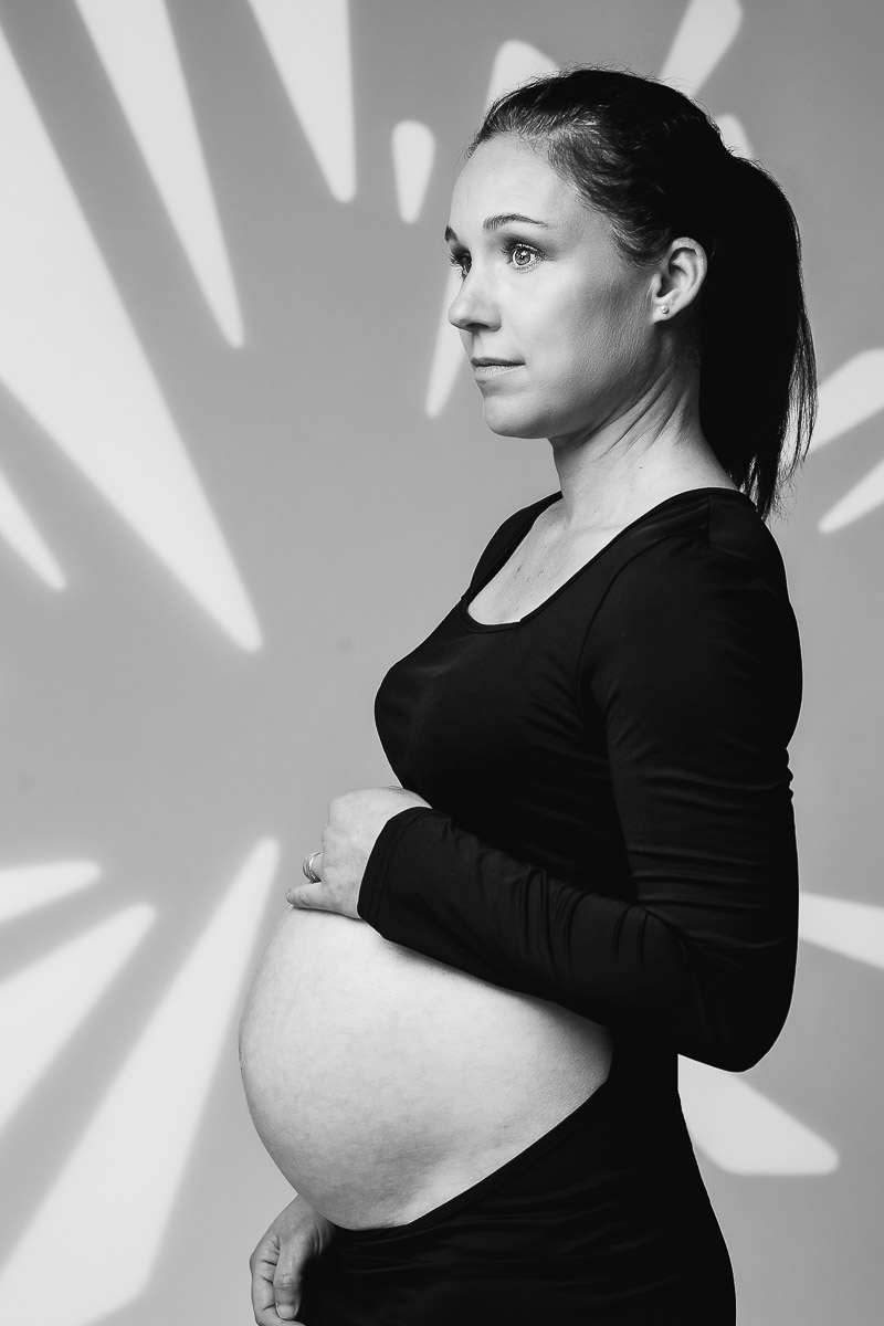Portrait de grossesse en noir et blanc avec des ombres de feuilles sur le fond au studio elisa abron près d'Angers